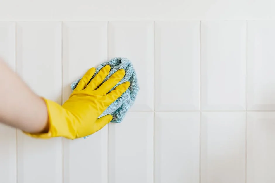 Anonymous person in yellow rubber gloves using simple sponge for cleaning mirror in bathroom